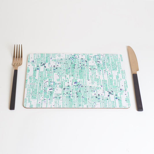 A rectangular placemat with a green and blue pattern of dots and splashes, placed on a white background with a fork on the left side and a knife on the right side.
