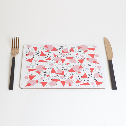 A rectangular placemat with a geometric pattern of red triangles and curvy lines in pink, black, and grey, displayed on a white background, accompanied by a fork and knife.