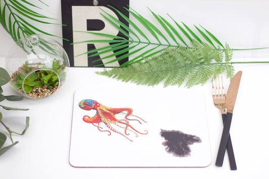 A decorative placemat featuring an artistic depiction of an octopus with ink, placed on a table with a plant, a fork, and a coaster.