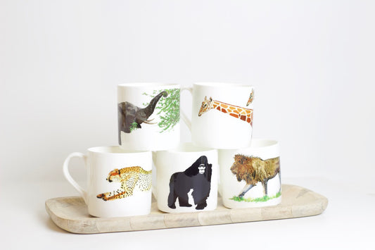 A set of bone china mugs with various animal designs, including a lion, gorilla, elephant, two giraffes, and a cheetah, displayed on a wooden tray against a white background.