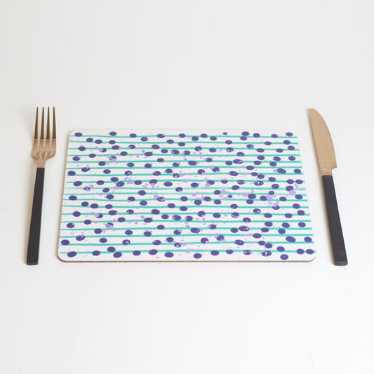 A rectangular placemat with a green and blue dot pattern, featuring a fork on the left side and a knife on the right side, placed on a white background.