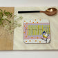 Coaster with a bird design on a wooden board with a spoon and flowers.