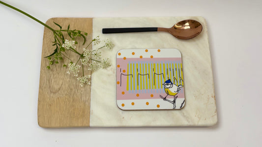 Coaster with a bird design on a wooden board with a spoon and flowers.