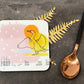 Coaster with duck illustration on a dark surface with a spoon and decorative leaves