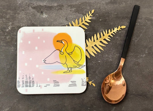 Coaster with duck illustration on a dark surface with a spoon and decorative leaves