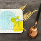 Coaster with bird design on a dark surface with a spoon and leaf