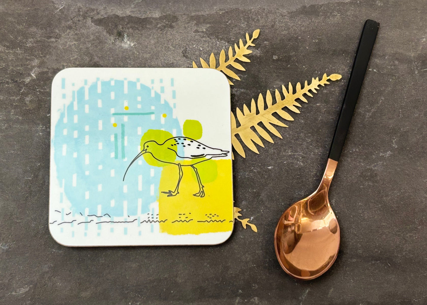 Coaster with bird design on a dark surface with a spoon and leaf