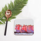 Coaster with colorful design, spoon, and fern on a white background