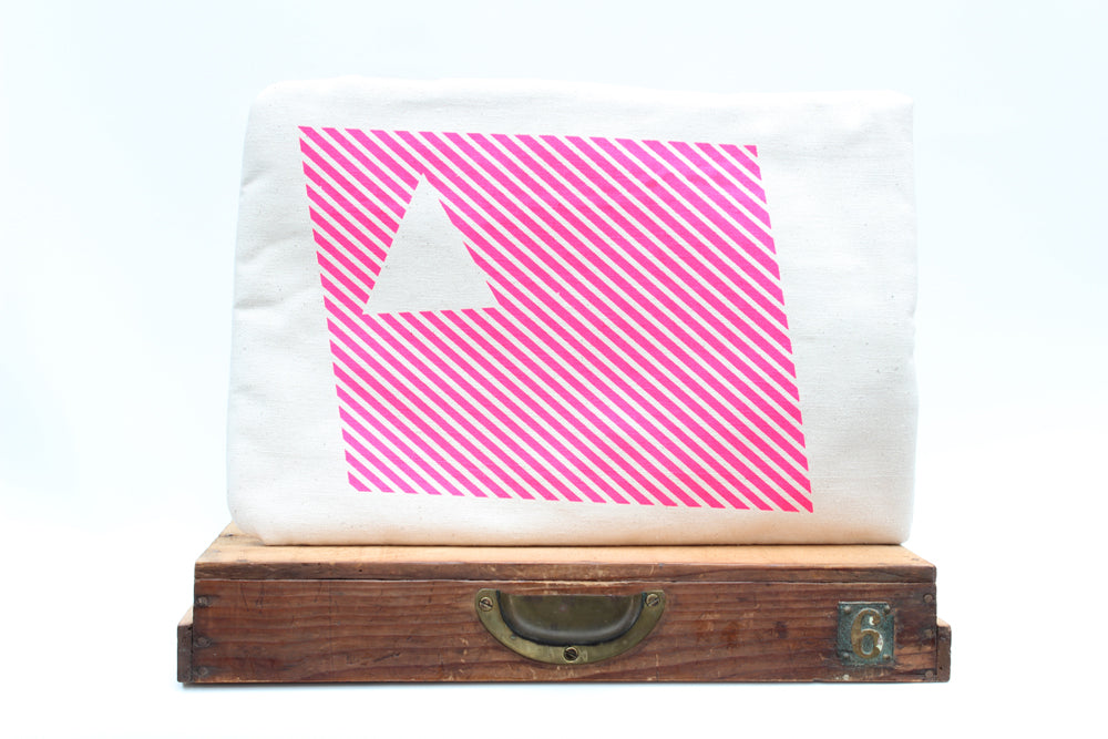 White leptop sleeve with pink diagonal stripes and a white triangle on a wooden surface.