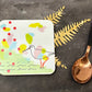 Coaster with a colorful bird design on a dark surface with a spoon and gold leaves.