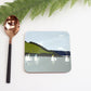 Coaster with sailboat design on a white surface with a copper spoon and greenery.