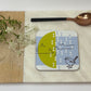 Coaster with bird design on a marble and wood surface with a spoon and flowers.