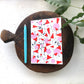 A6 notebook with a geometric pattern in red and white colors, placed on a wooden board next to a blue pen.