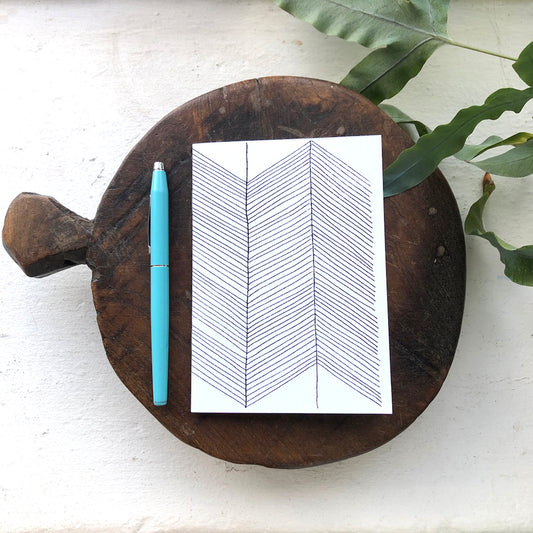 A6 notebook with a geometric pattern on the cover, a pen, and a plant leaf on a wooden surface.