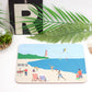 A colorful beach-themed placemat with a design that includes beach chairs, an umbrella, and a fishing line, positioned on a table with a fork and a knife to the side.