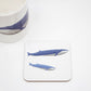A square coaster with a cork base featuring a hand-drawn design of a blue whale and her calf, accompanied by a white mug with a similar design.