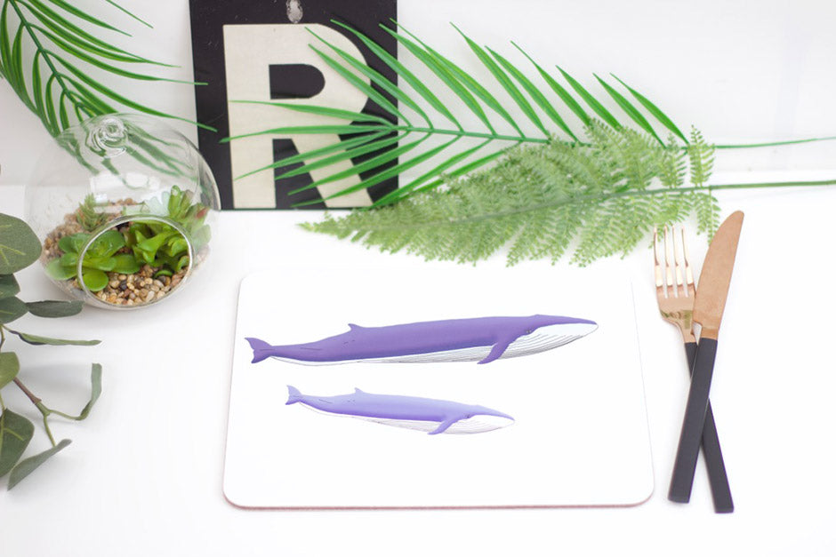 A placemat with an illustration of blue whales, alongside a fork, knife, and a decorative plant.