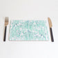 A rectangular placemat with a green and blue pattern of dots and splashes, placed on a white background with a fork on the left side and a knife on the right side.