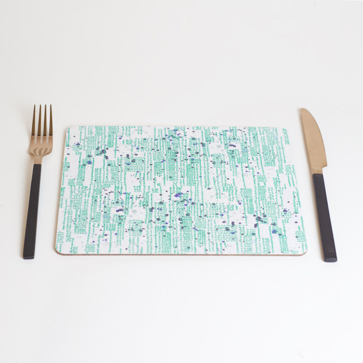 A rectangular placemat with a green and blue pattern of dots and splashes, placed on a white background with a fork on the left side and a knife on the right side.