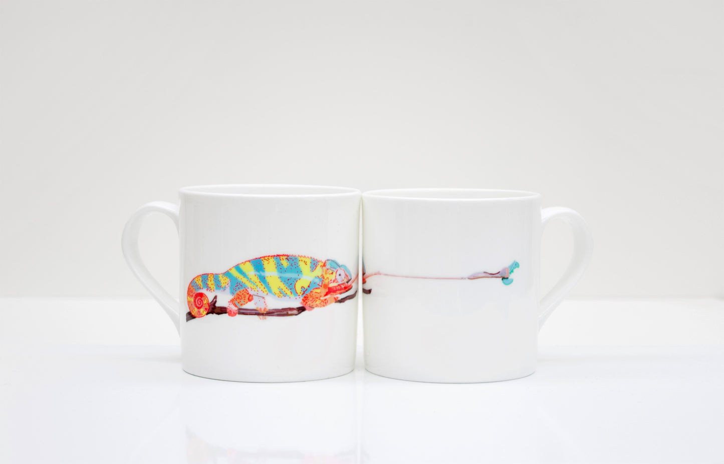 Two white bone china mugs with a hand-drawn design of a chameleon and a caterpillar around the mug.