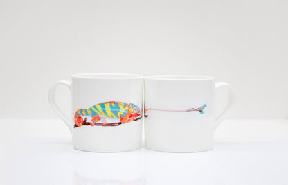 Two white bone china mugs with a hand-drawn design of a chameleon and a caterpillar around the mug.