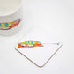 A square coaster with a hand-drawn chameleon design from the Jungle Collection, placed on a white surface next to a white mug with a similar design.