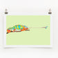 A colorful digital print of a chameleon on a lime background, displayed with clips on a white wall.