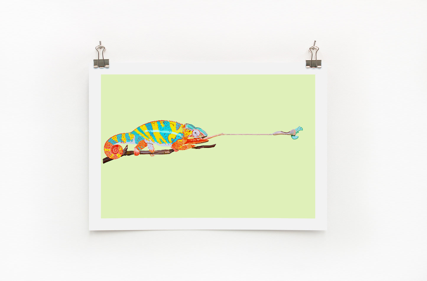 A colorful digital print of a chameleon on a lime background, displayed with clips on a white wall.