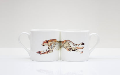 Two white bone china mugs with a cheetah design in the center, placed on a white surface.