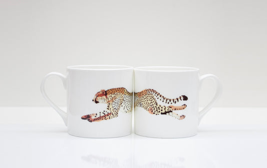 Two white bone china mugs with a cheetah design in the center, placed on a white surface.