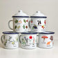 A collection of enamel mugs with various illustrations of plants and fungi, each with a blue rim and lid, displayed against a white background.