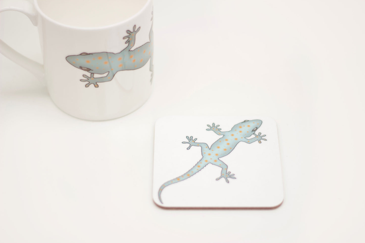 A square coaster with a design of a gecko climbing across it.