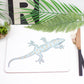 A placemat featuring a drawing of a gecko, with a jungle-themed decoration in the background including a palm leaf and greenery.