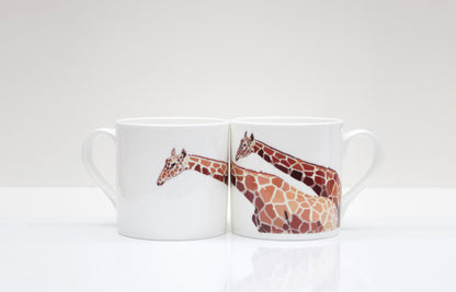 A set of two white bone china mugs with a hand-drawn giraffe design in brown and beige tones, placed on a white surface.