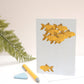 A greetings card with an illustration of goldfish swimming against a blue background, placed on a white surface with a pencil and a green leaf to the side.