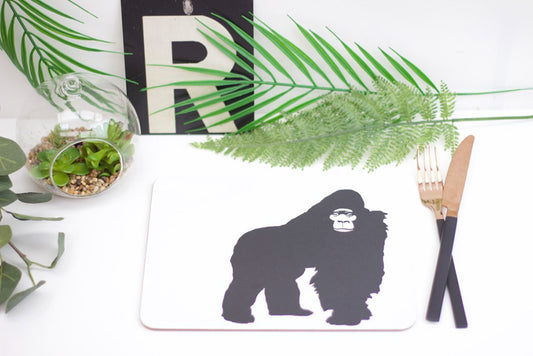 A placemat with a gorilla in the center, placed on a table with cutlery on the right and a green plant in the background.