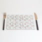 A rectangular placemat with a geometric pattern of overlapping shapes and colors, displayed on a white background. A fork and knife are placed on top of the placemat.
