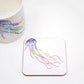 A hand-drawn jellyfish design on a coaster, with a white mug with same design visible in the background.