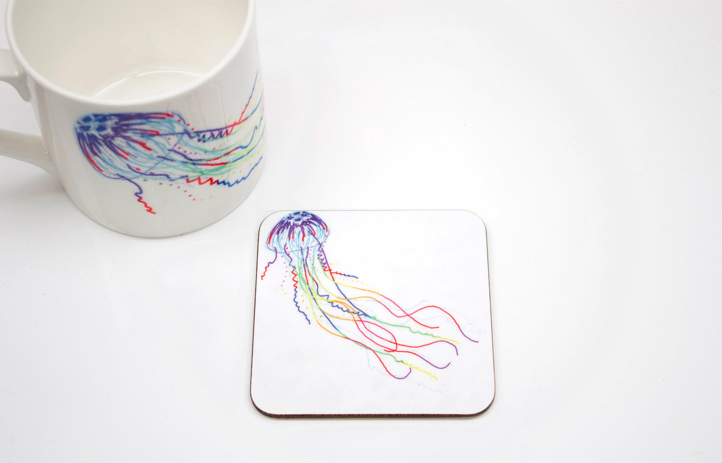A hand-drawn jellyfish design on a coaster, with a white mug with same design visible in the background.