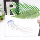 A placemat with a jellyfish design, part of the underwater collection, displayed on a table with a plant, a coaster, and a brush.