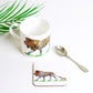 A coaster with a hand-drawn design of a lion and its cub on it, part of the Africa Collection. The coaster is accompanied by a spoon and there's a palm leaf in the background.