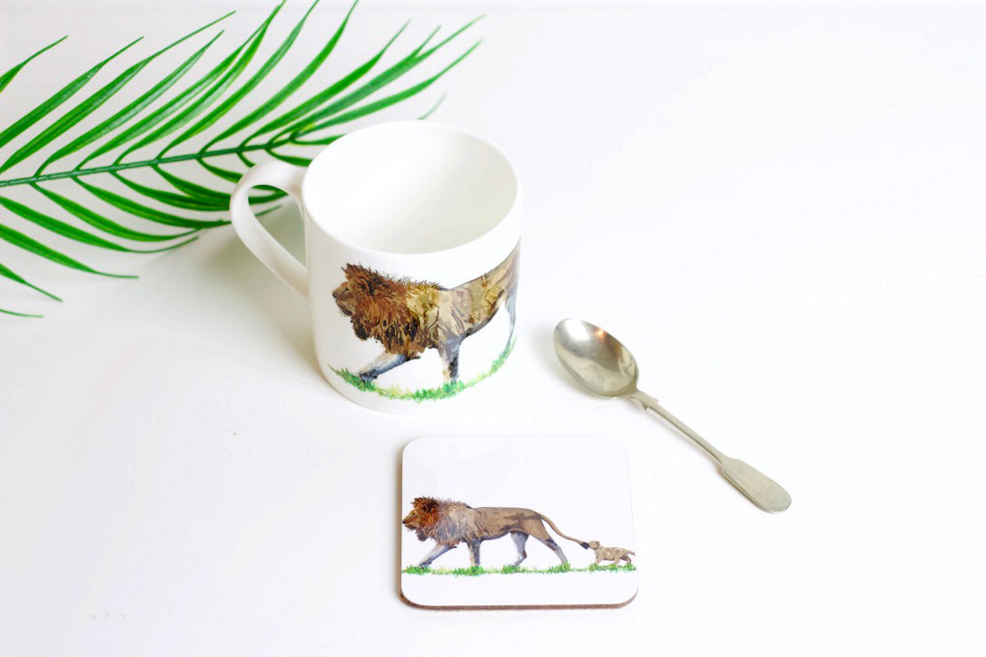 A coaster with a hand-drawn design of a lion and its cub on it, part of the Africa Collection. The coaster is accompanied by a spoon and there's a palm leaf in the background.