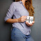 A person holding a bone china mug with a geometric pattern, specifically a cross, on a blue and white striped background.