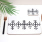 A white and black geometric symbol on a rectangle  placemat which is displayed on a table with a fork, knife, and a napkin. There is a palm leaf in the background.