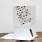 A greeting card with a geometric pattern and the text 'CONGRATULATIONS ON YOUR NEW HOME!' written on it. The card is accompanied by an envelope placed on a wooden surface.