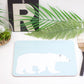 A light blue placemat with a polar bear design, displayed on a table with cutlery and a plant in the background.