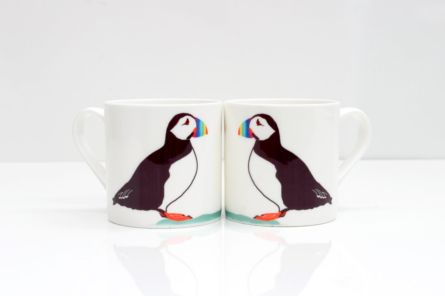 Two bone china mugs puffin designs, one mug showing the front side with the puffin, and the other mug showing the back side. Both mugs have a white color scheme and a reflective surface.