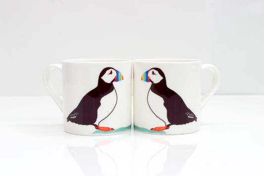 Two bone china mugs puffin designs, one mug showing the front side with the puffin, and the other mug showing the back side. Both mugs have a white color scheme and a reflective surface.