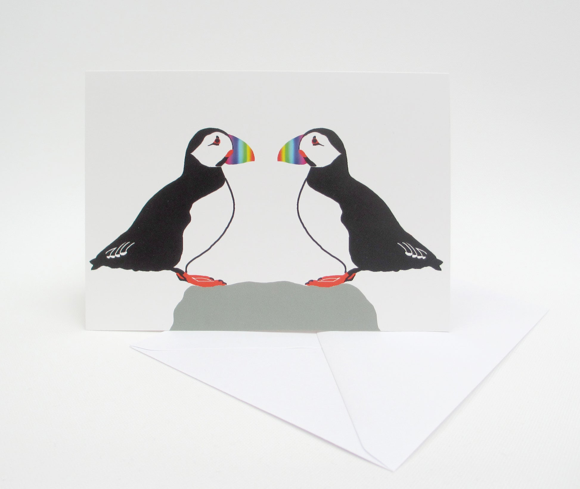 A greeting card with a illustration of two puffins facing each other. The card is set against a white background and there is a white envelope included.