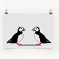 A digital print featuring two puffins with colorful rainbow beaks. The background is plain white.